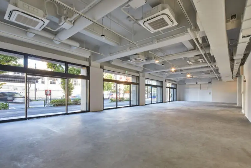 - 広々とした商業スペース、コンクリート床と大きな窓から自然光が入る明るい室内、天井には空調設備が設置されている