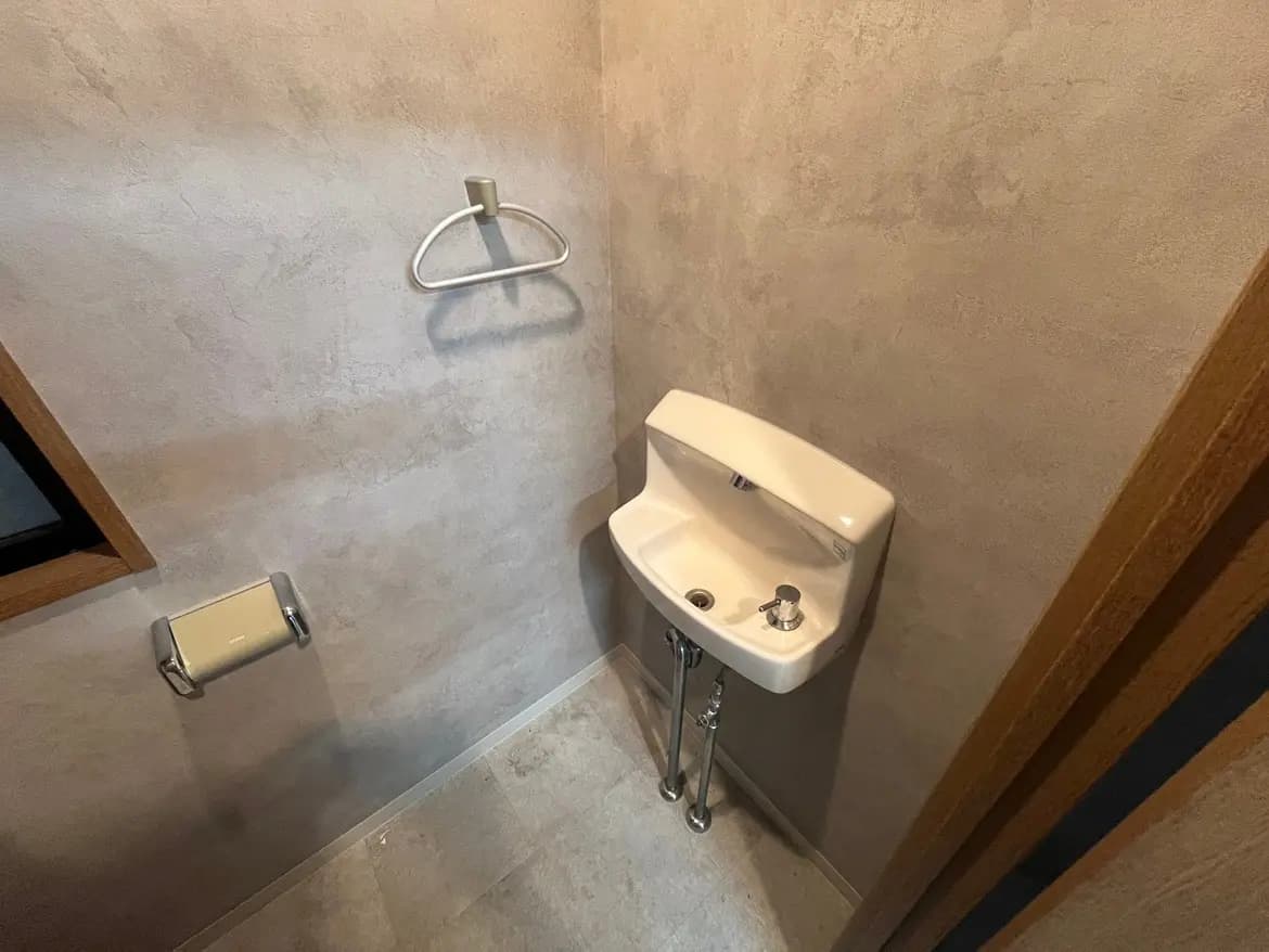 - シンプルでスタイリッシュな扁平タイプの洗面台、グレーの壁とテラコッタ調の床材、トイレットペーパーラックがあるトイレの内部