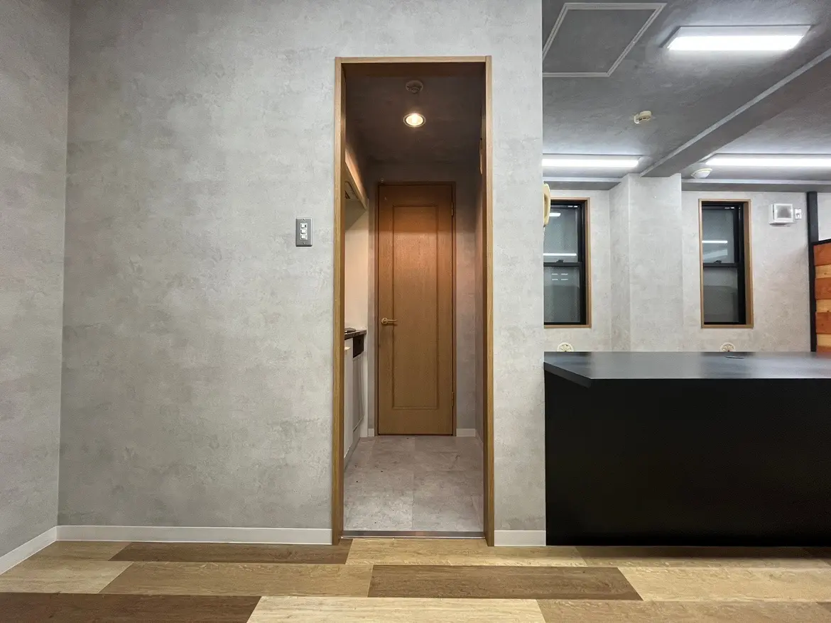- シンプルでモダンなインテリアデザインの部屋、木製のフローリングと黒いカウンター、壁に開いたドアが特徴の空間