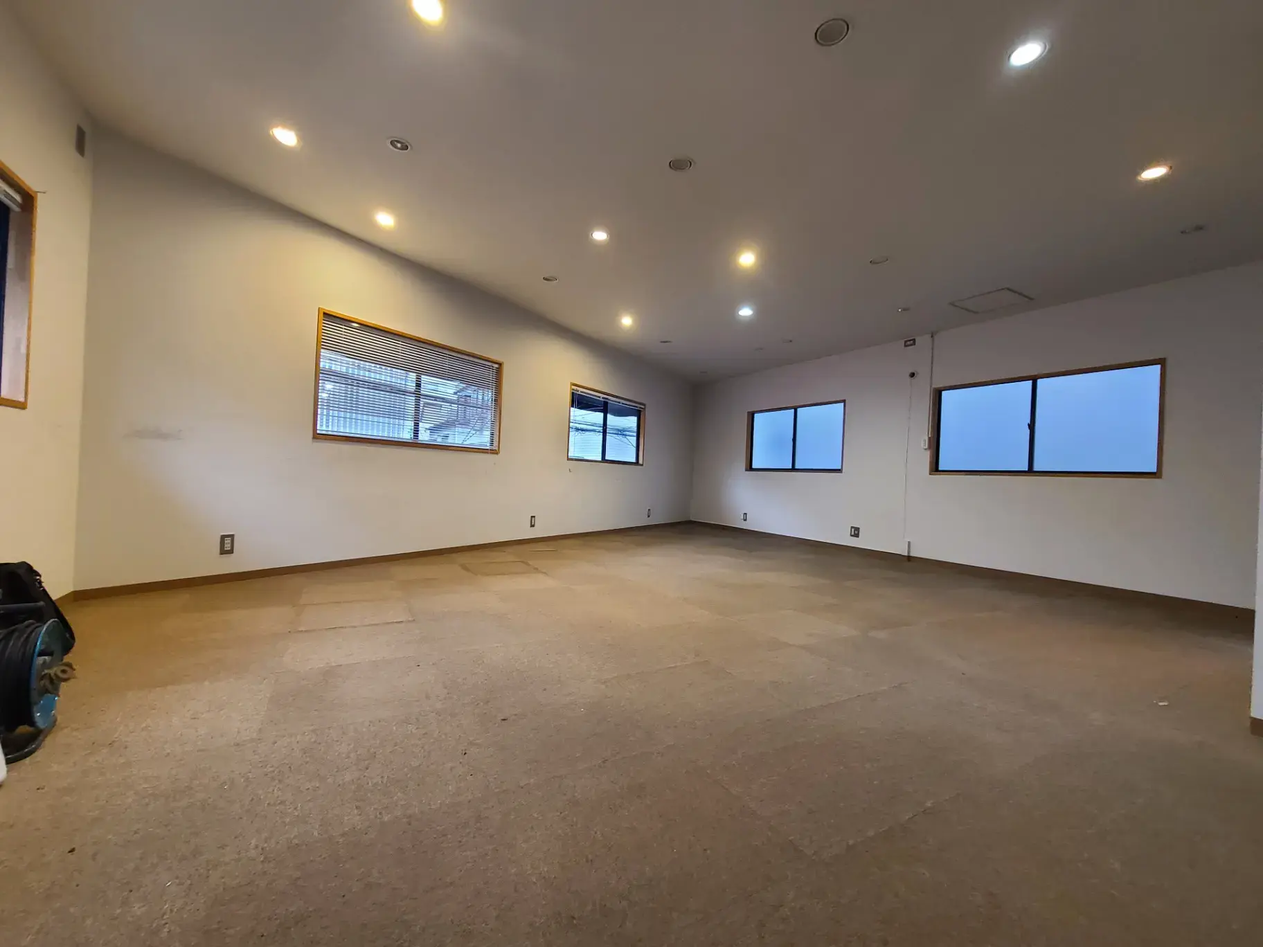 空間の広さを感じさせるシンプルな内装の無垢材フローリングの部屋、ダウンライトと自然光で明るい空間