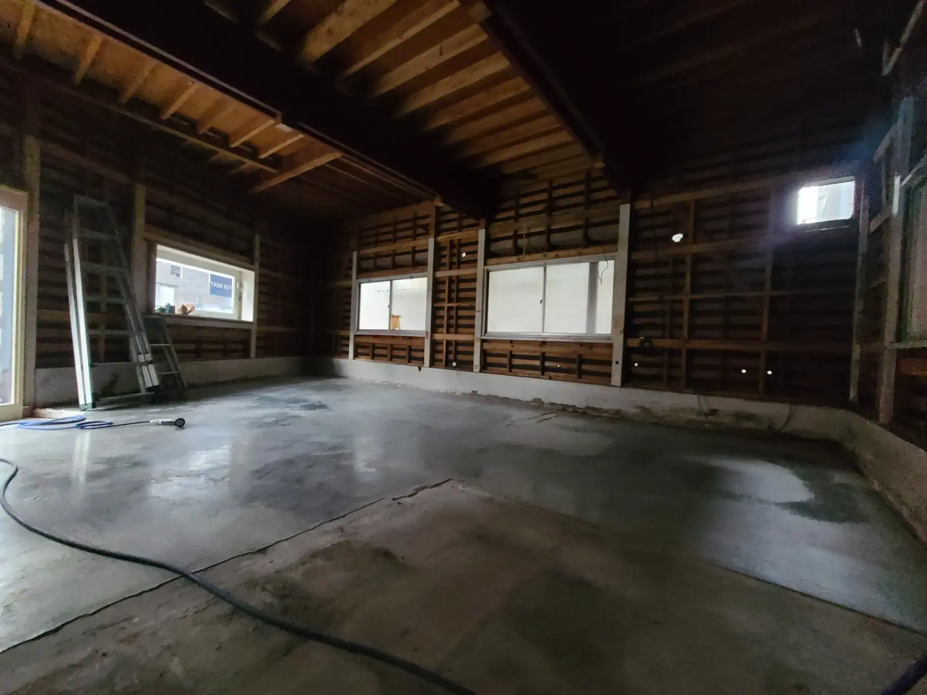 改装前の古い車庫の内部、コンクリートの床と木造の壁、梯子と窓